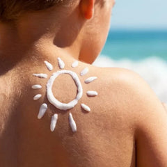 A child with sunscreen applied in a sun shape on their back at the beach, promoting sun safety.